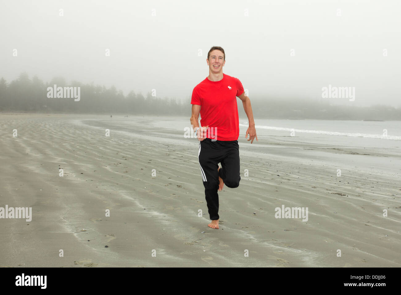 Teenage boy running on Chesterman Beach on foggy day-Tofino, British Columbia, Canada. Stock Photo