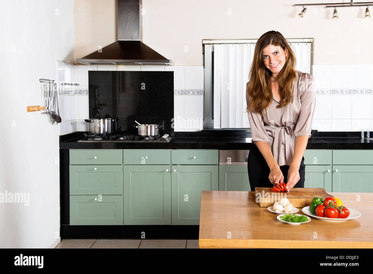 Portrait of beautiful young businesswoman chopping vegetables at kitchen counter Stock Photo