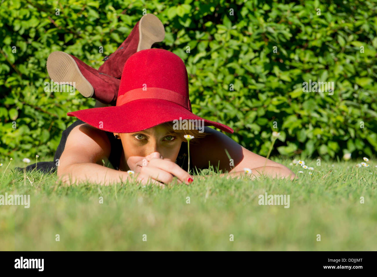 Young, classy woman, picking a single daisy, whilst laying on the grass on a beautiful summer afternoon Stock Photo