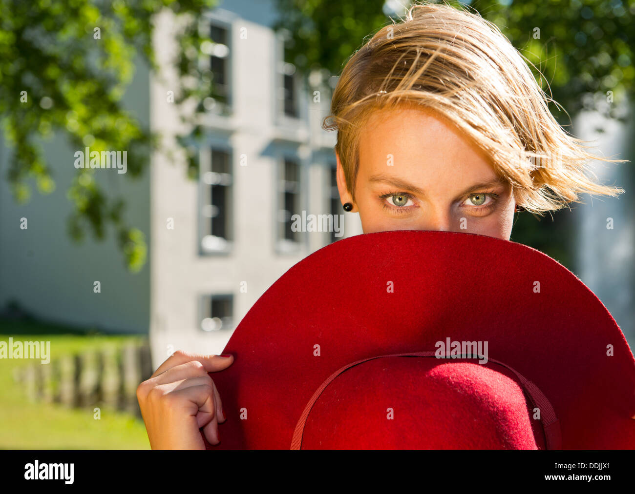 Young woman partially hiding behind a red, felt hat on a warm summer day Stock Photo