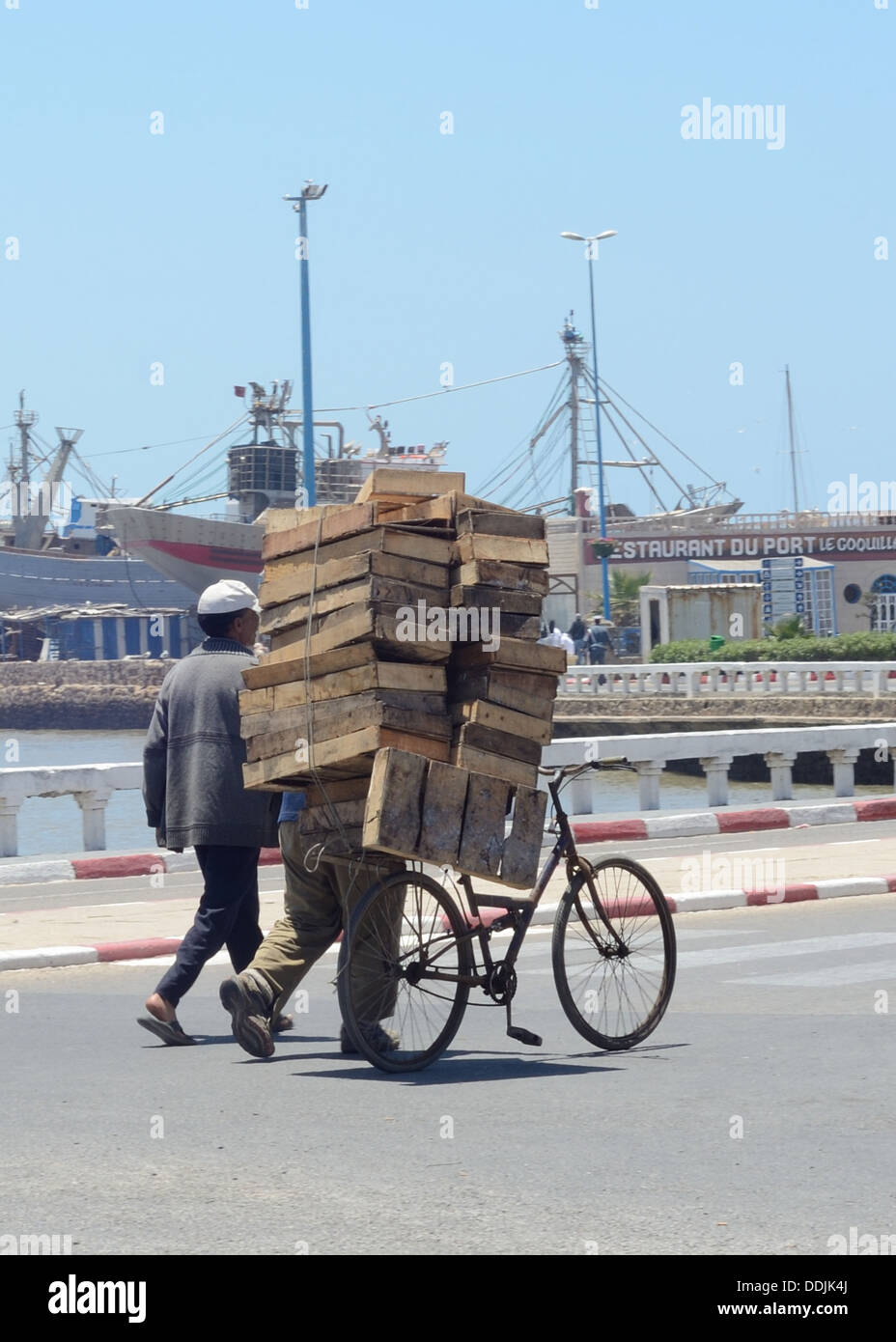 Two men pushing wooden pallets on a bike down a road Stock Photo