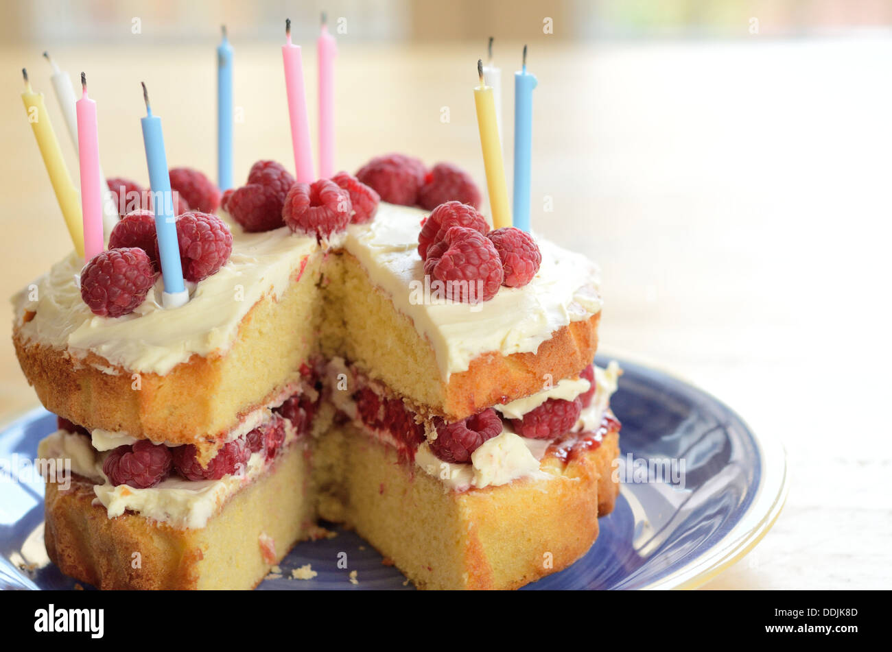 Birthday Cake homemade with sponge, raspberries, cream and candles on a blue plate and wooden table Stock Photo