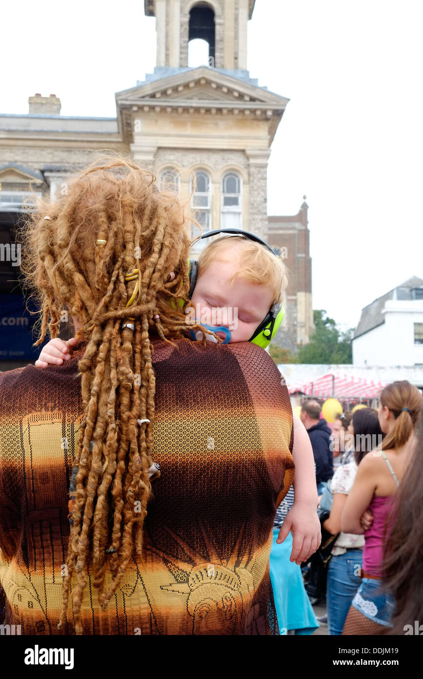 A young boy, cradled in the arms of his dreadlocked Dad, takes a quick nap wearing his ear protectors at Kingston Carnival 2013. Stock Photo