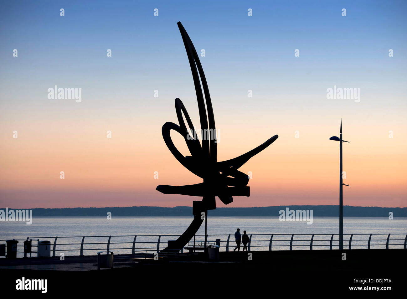 Port Talbot - South Wales - UK - 3rd September 2013 : People walking past the "Kite Trail" sculpture as the sun sets along the seafront at Aberavon Beach near Port Talbot this evening. The Kite Trail sculpture at Aberavon seafront is Wales' largest sculpture standing at 12 metres high and weighing 11 tonnes. It was designed by Carmarthenshire-based artist and sculptor Andrew Rowe and was installed in December 2007. © Phil Rees/Alamy Live News Stock Photo