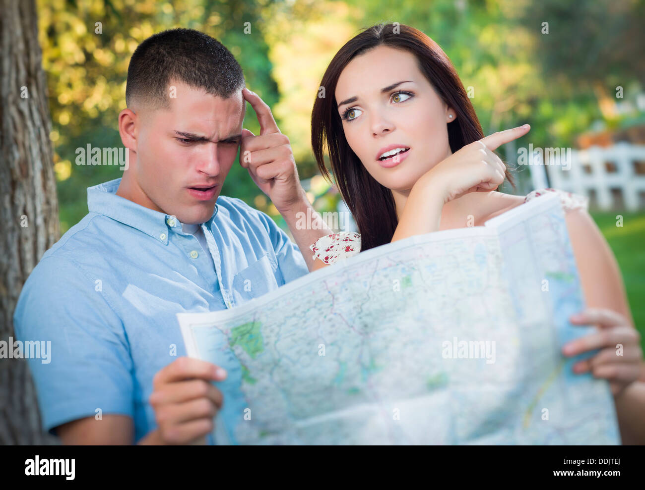 Lost and Confused Mixed Race Couple Looking Over A Map Outside Together. Stock Photo