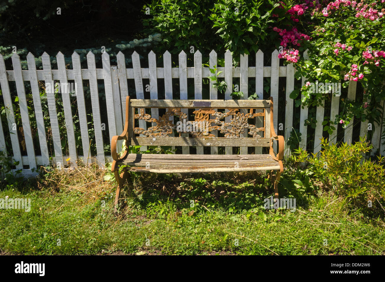 old weather beaten park bench in front of white picket fence in Niagara-on-the-Lake, Ontario, Canada Stock Photo