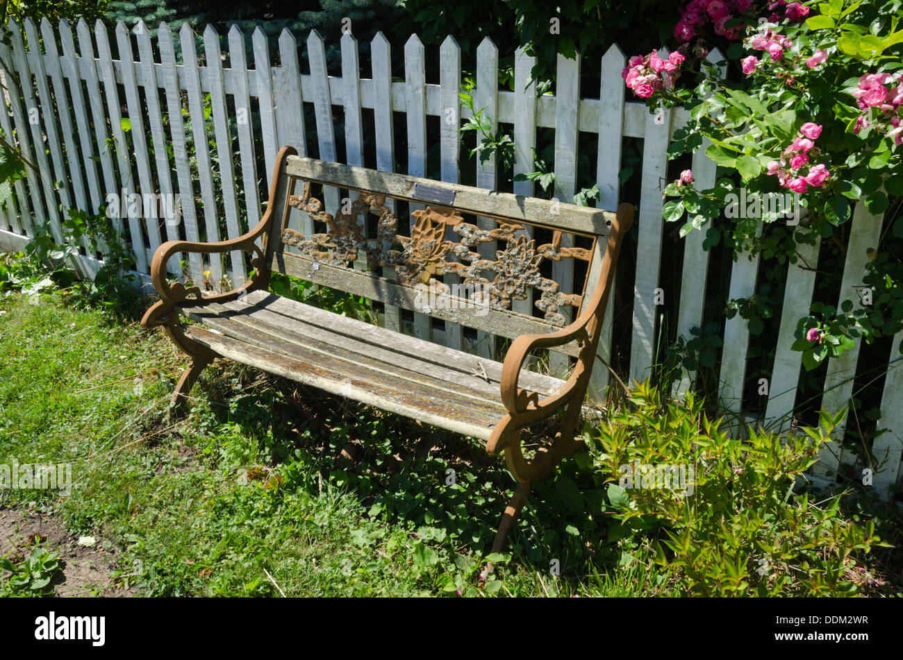old weather beaten park bench in front of white picket fence in Niagara-on-the-Lake, Ontario, Canada Stock Photo