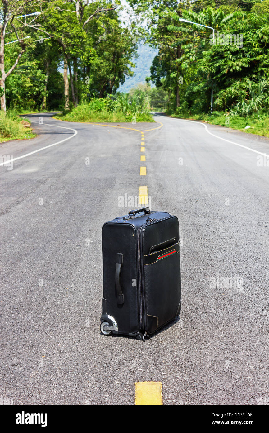 lone suitcase stands in the middle of the road Stock Photo