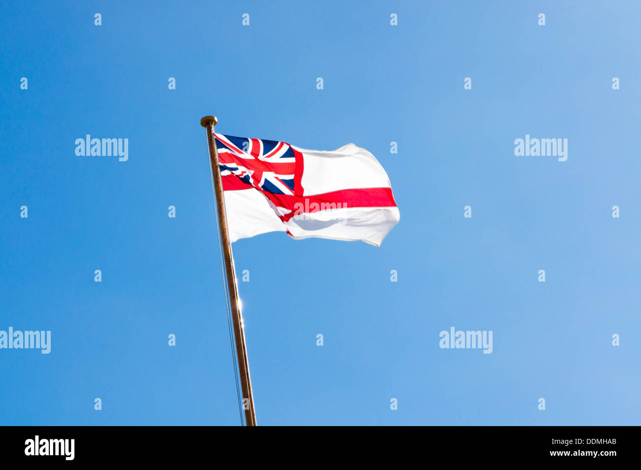 Royal Navy White ensign flies against a blue sky Stock Photo