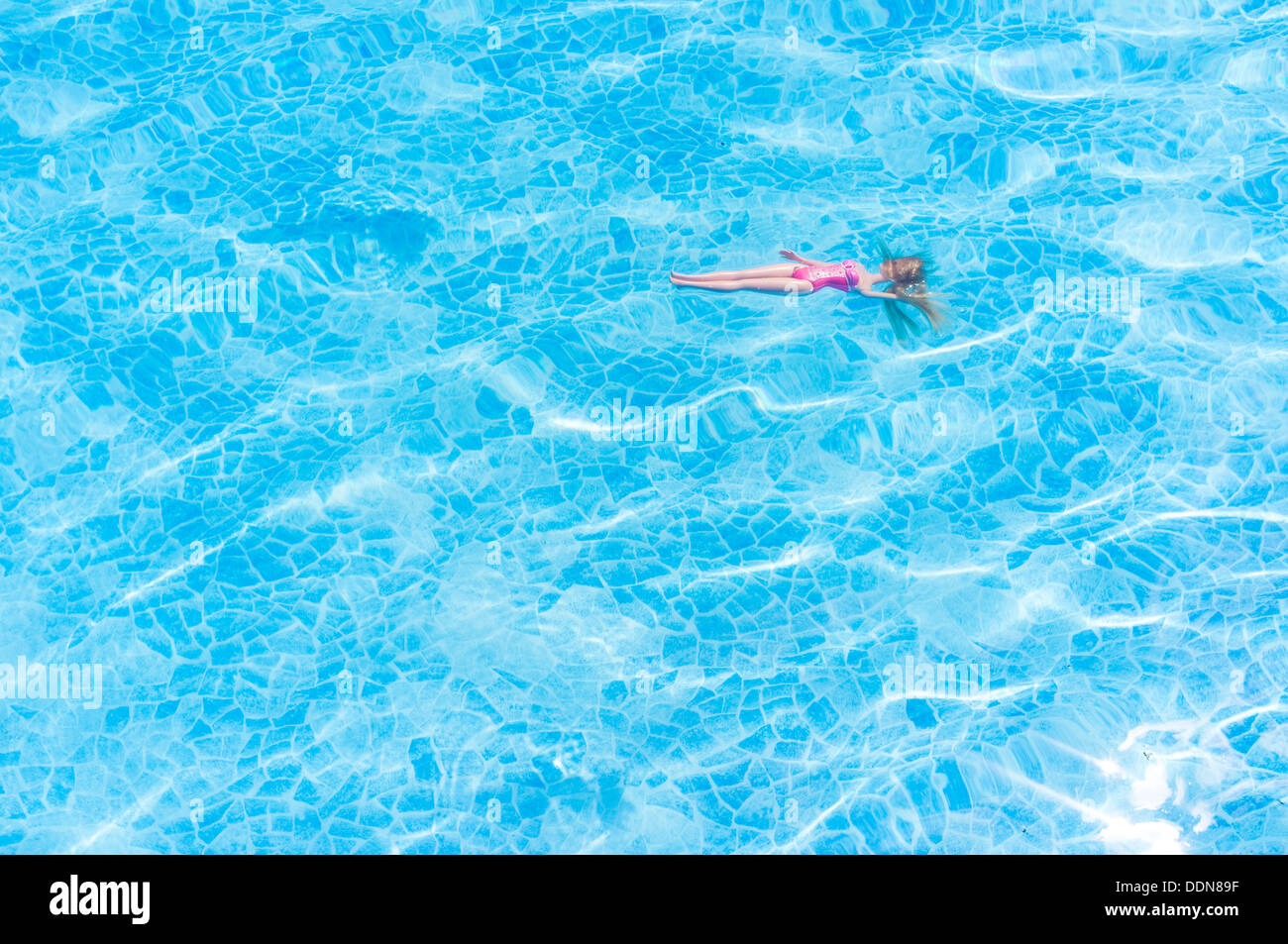 A toy figure doll in pink, floating in blue swimming pool in a sunny day Stock Photo