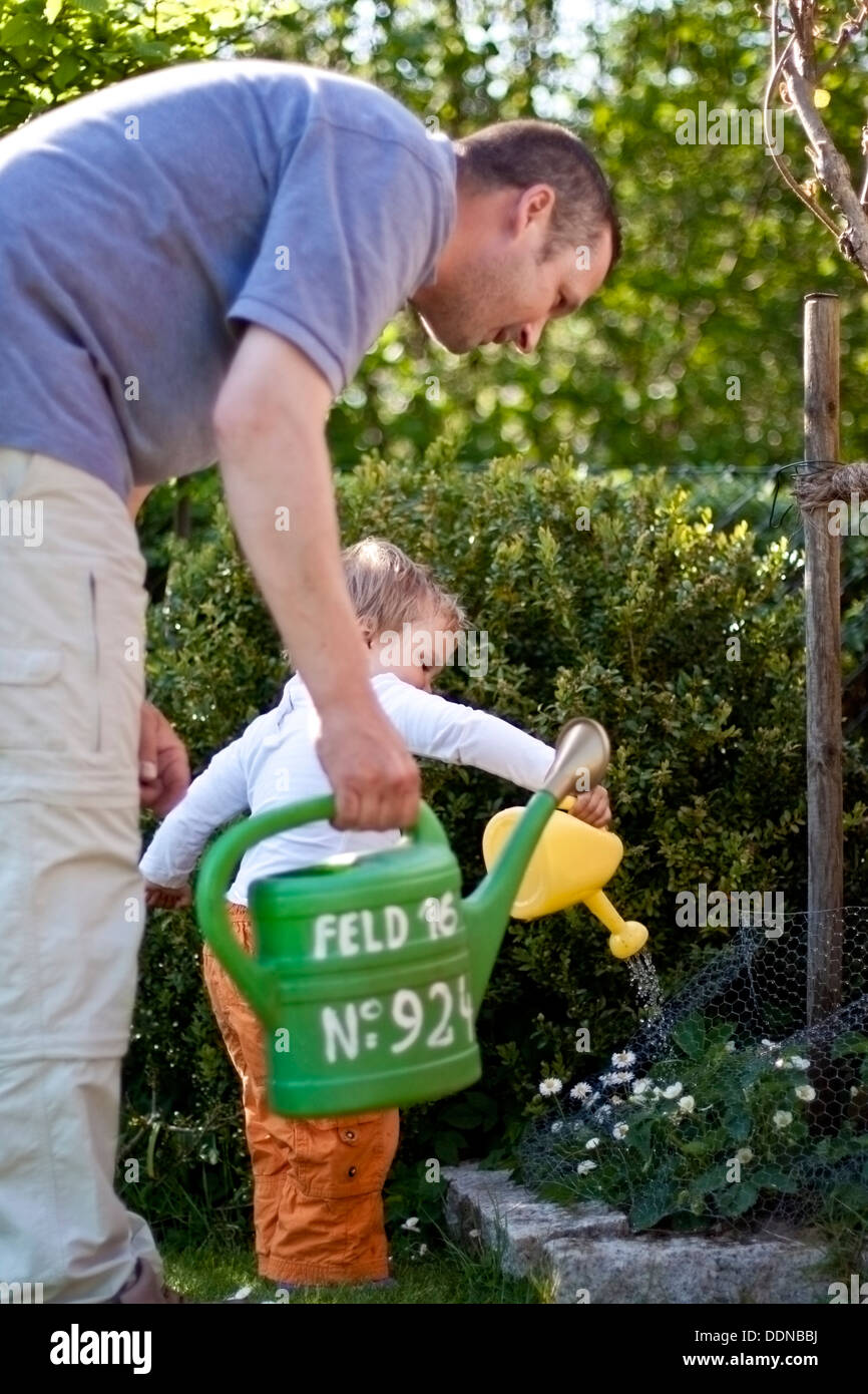 Toddler with father in garden watering flowers Stock Photo