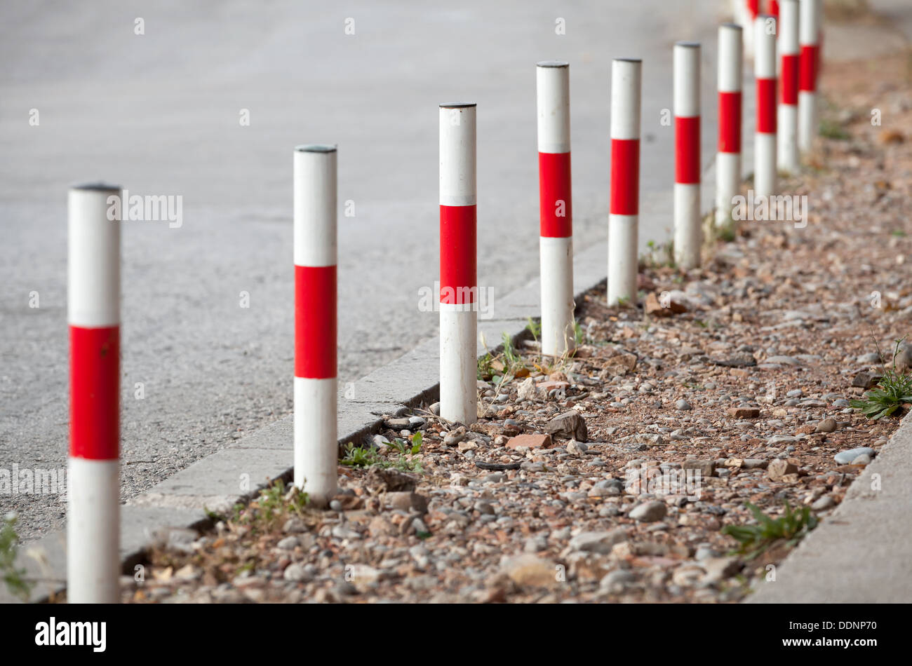 Striped red and white signal poles stand on asphalt roadside Stock Photo