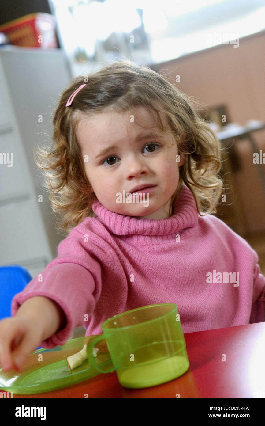 three-year-old-girl-with-a-plate-and-cup-looking-miserable-stock-photo