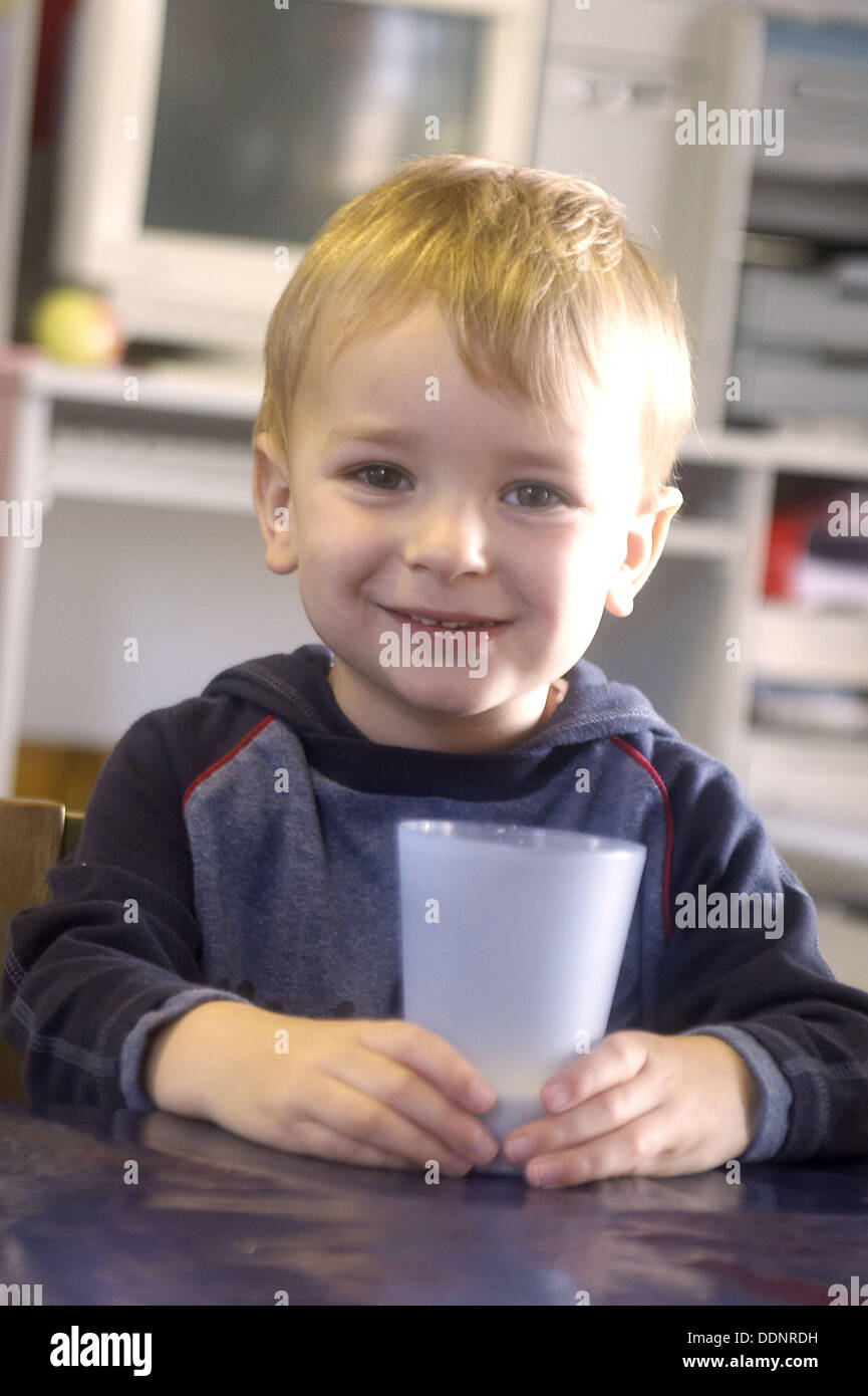 3 year old boy smiling into camera at nursery, holding a cup of milk