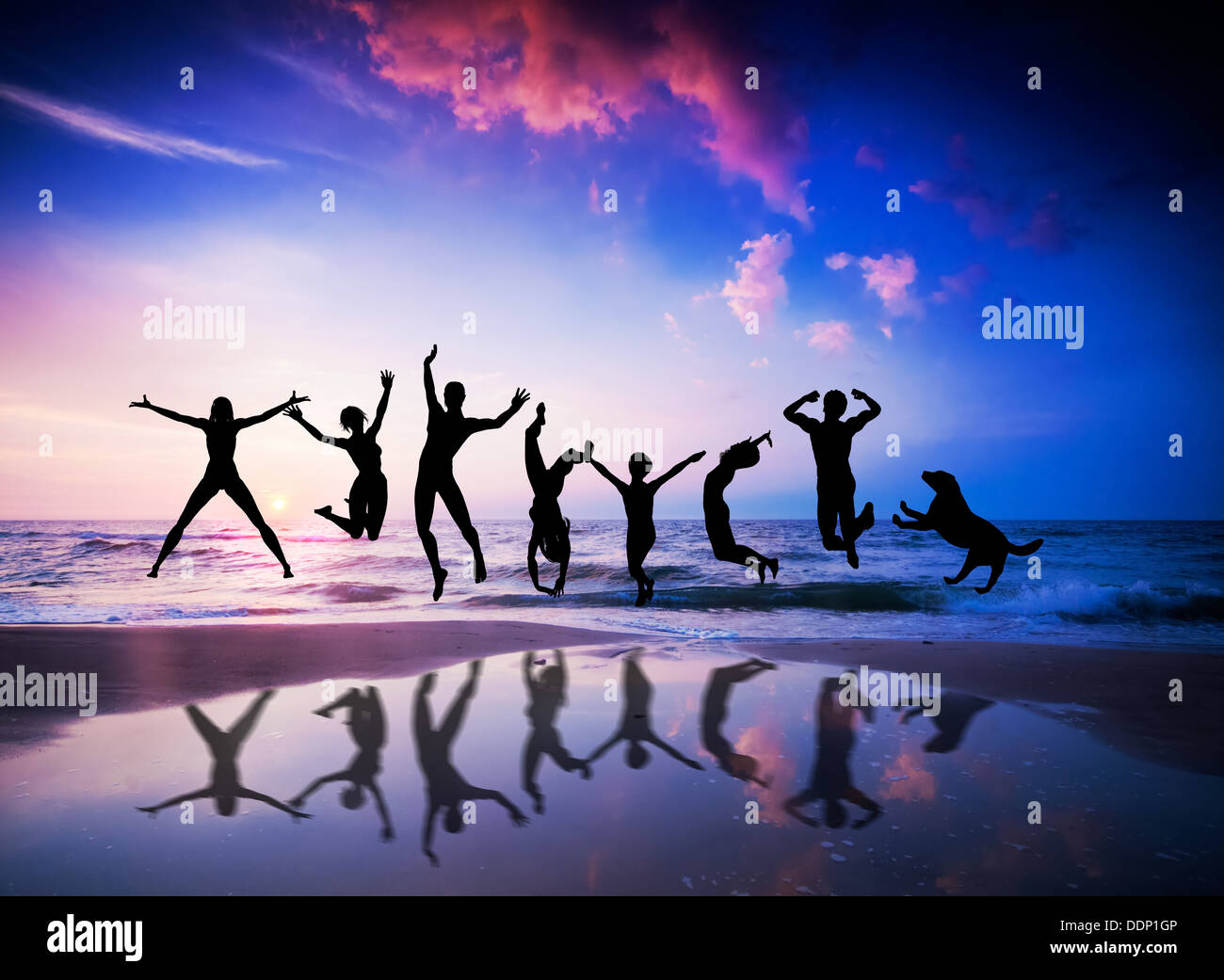 Happy people and dog jumping together on the sunset beach Stock Photo