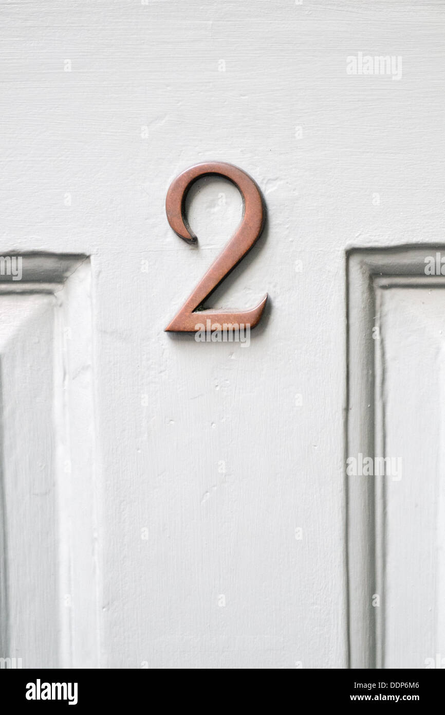 An unpolished brass number 2 on a white painted wood front door Stock Photo