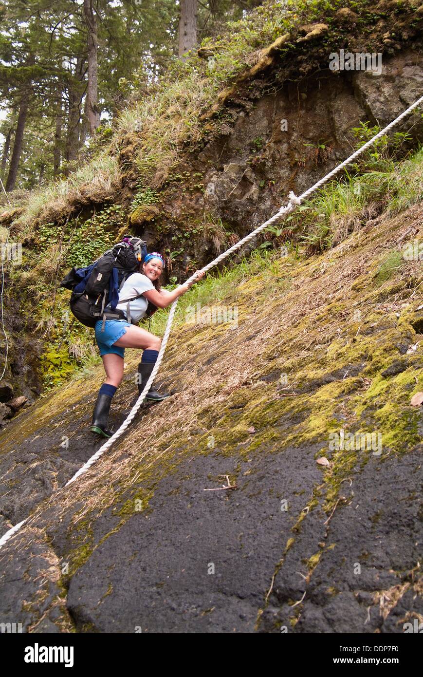 a hiker uses a rope to climb up a steep slope on Nootka Island, BC