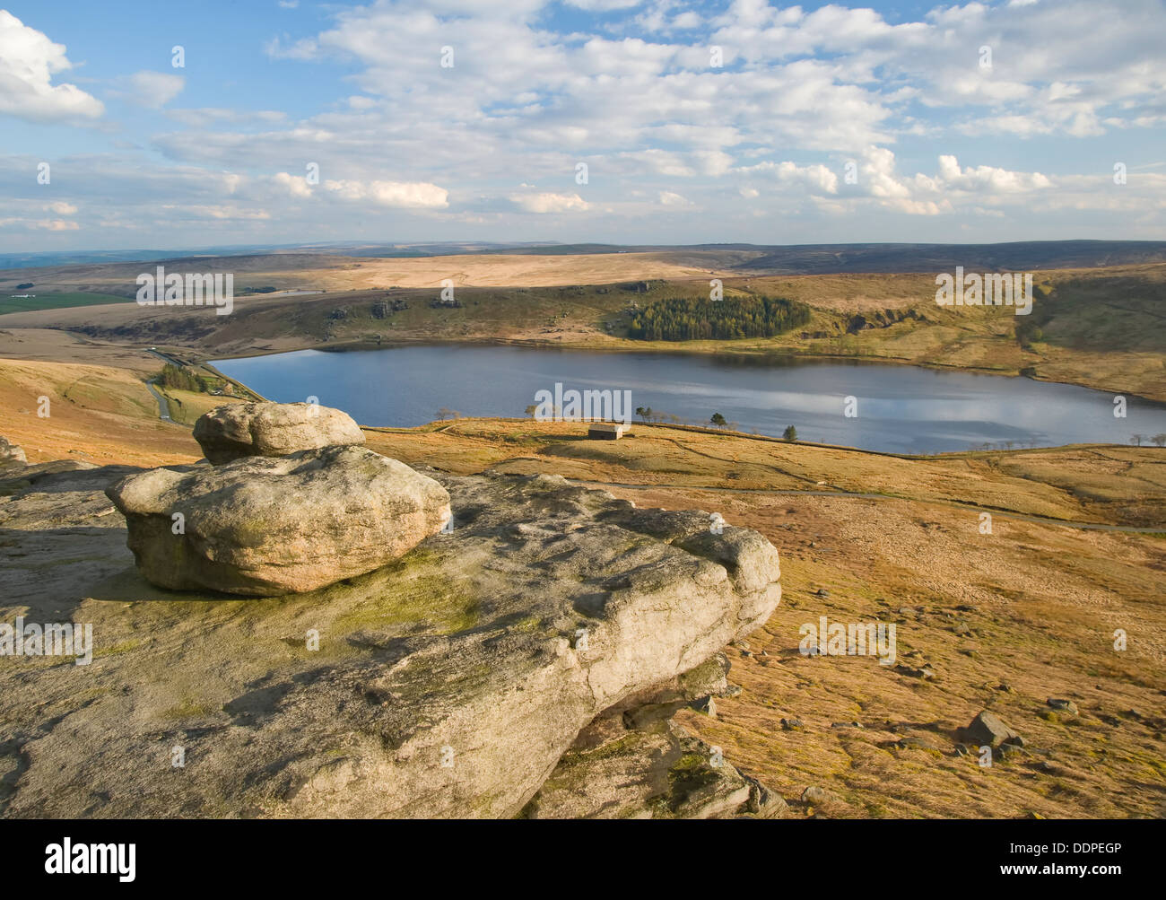 A wind shaped millstone grit boulder sits atop a windy ridge in Yorkshire overlooking a moorland reservoir. Stock Photo