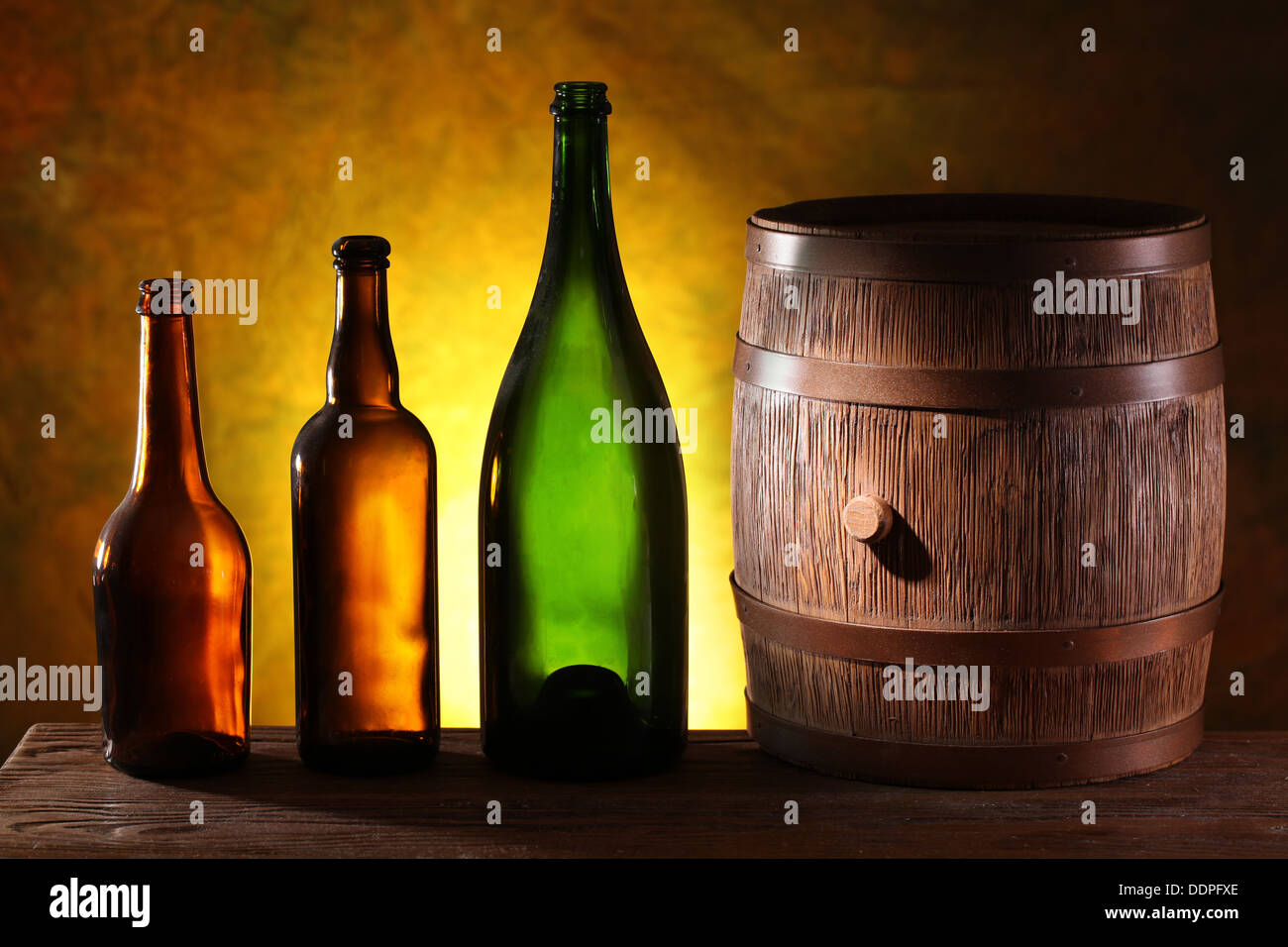 Wooden barrel with colors bottles on a dark yellow background. Stock Photo