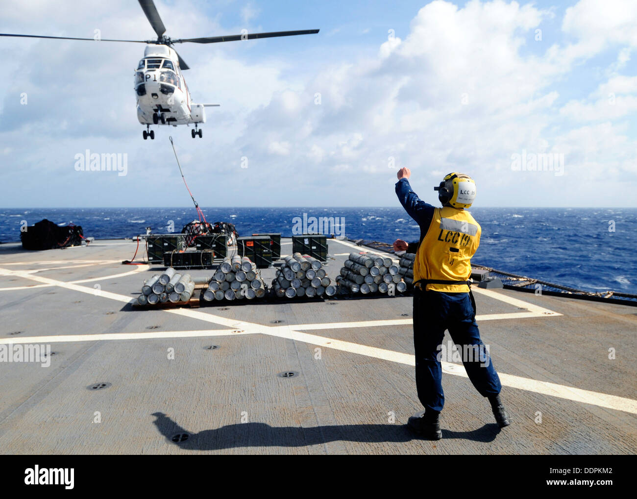 Boatswain's Mate 3rd Class Edward Kirtley signals to an helicopter carrying ammunition