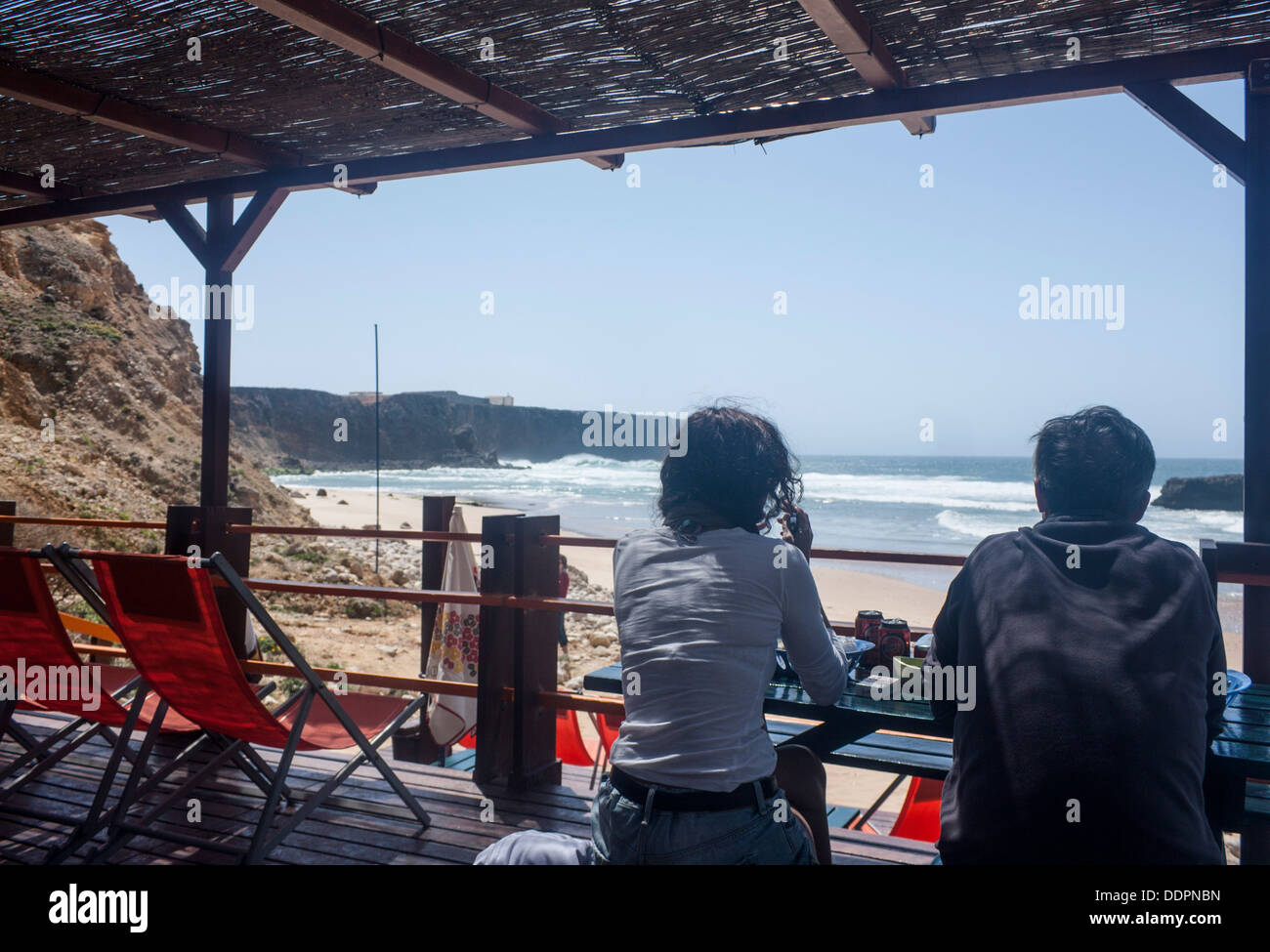 Two women sitting in cafe beach shack looking out to beach and sea ocean Praia do Tonel Sagres Costa Vicentina Algarve Portugal Stock Photo
