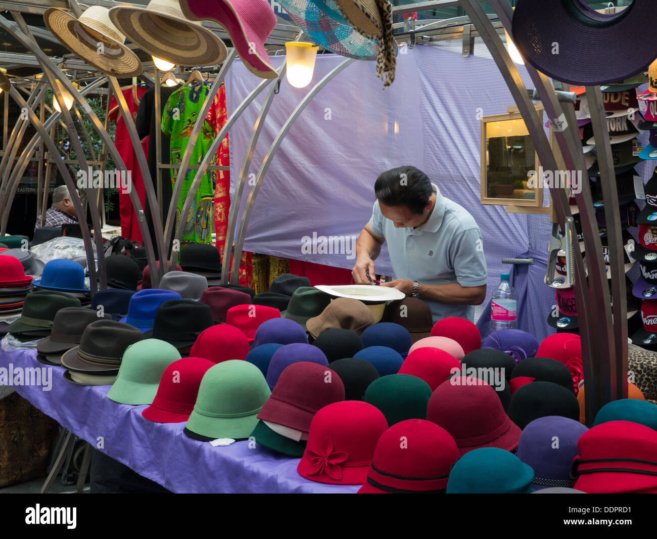 A man making and selling colourful hats at a market in London Stock