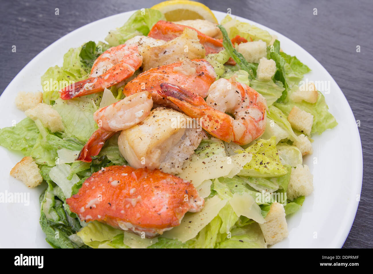 Caesar Salad with Prawns Salmon White Cod Fish Croutons Lemon and Cracked Black Pepper Closeup Stock Photo