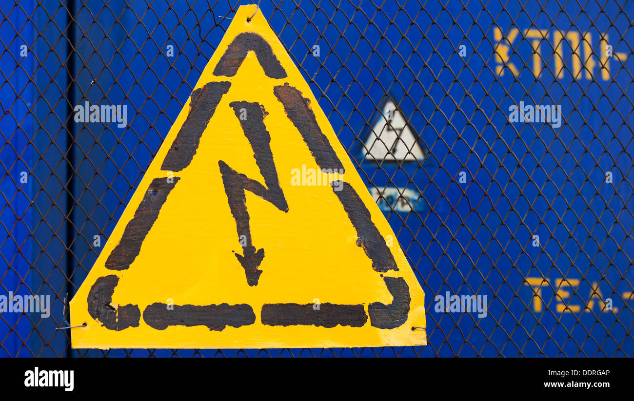 High voltage yellow sign mounted on blue metal rabitz grid with blue metal wall on background Stock Photo