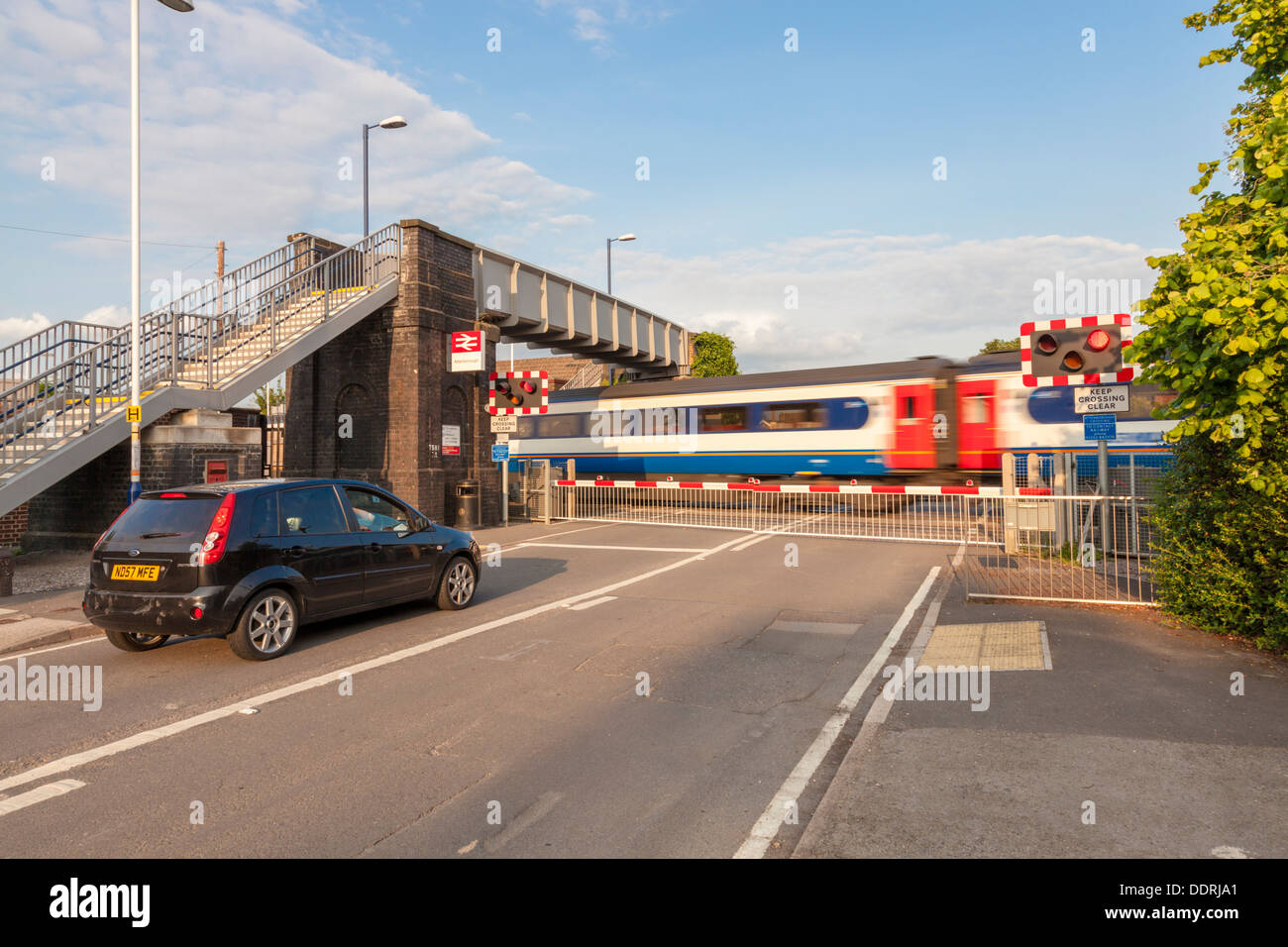 Car waiting at a level crossing with the barriers lowered as a train passes. Attenborough Railway Station, Nottinghamshire, England, UK Stock Photo