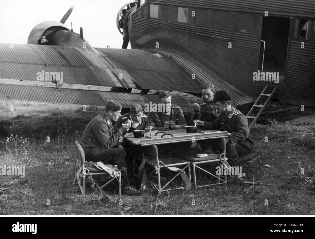 Second World War / WWII,Greece,German war correspondents of 3rd Air Force War Correspondent Company,during dinner besides an transport aircraft Junkers Ju 52,near Salonika,April 1941,journalist,journalists,propaganda company,soldiers,soldier,people,men,man,aeroplane,airplane,airplanes,aeroplanes,airfields,airfield,airstrip,strip,airstrips,strips,Luftwaffe(German Air Force),meal,meals,mess kit,seats,airline seat,the Balkans,Balkans campaign,communications zone,back area,rear echelon,Georg Schödl,German Reich,Third Reich,Mac,Additional-Rights-Clearences-Not Available Stock Photo
