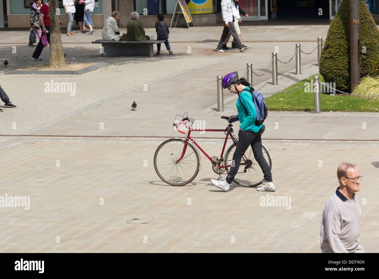 Woman wheeling her bike across the pedestrianised Victoria Square Bolton. Many riders fail to dismount in pedestrianised areas. Stock Photo