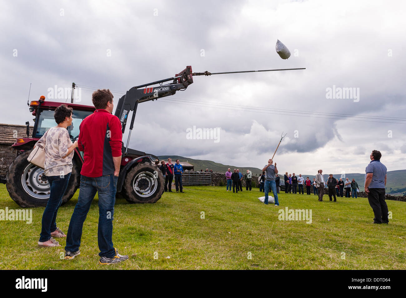 A man attempts to throw a bale of hay in a sack over a high pole in