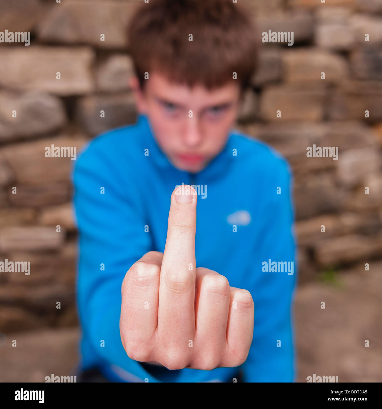 A 13 year old teenage boy being rude by sticking his middle finger up at the camera outside Stock Photo