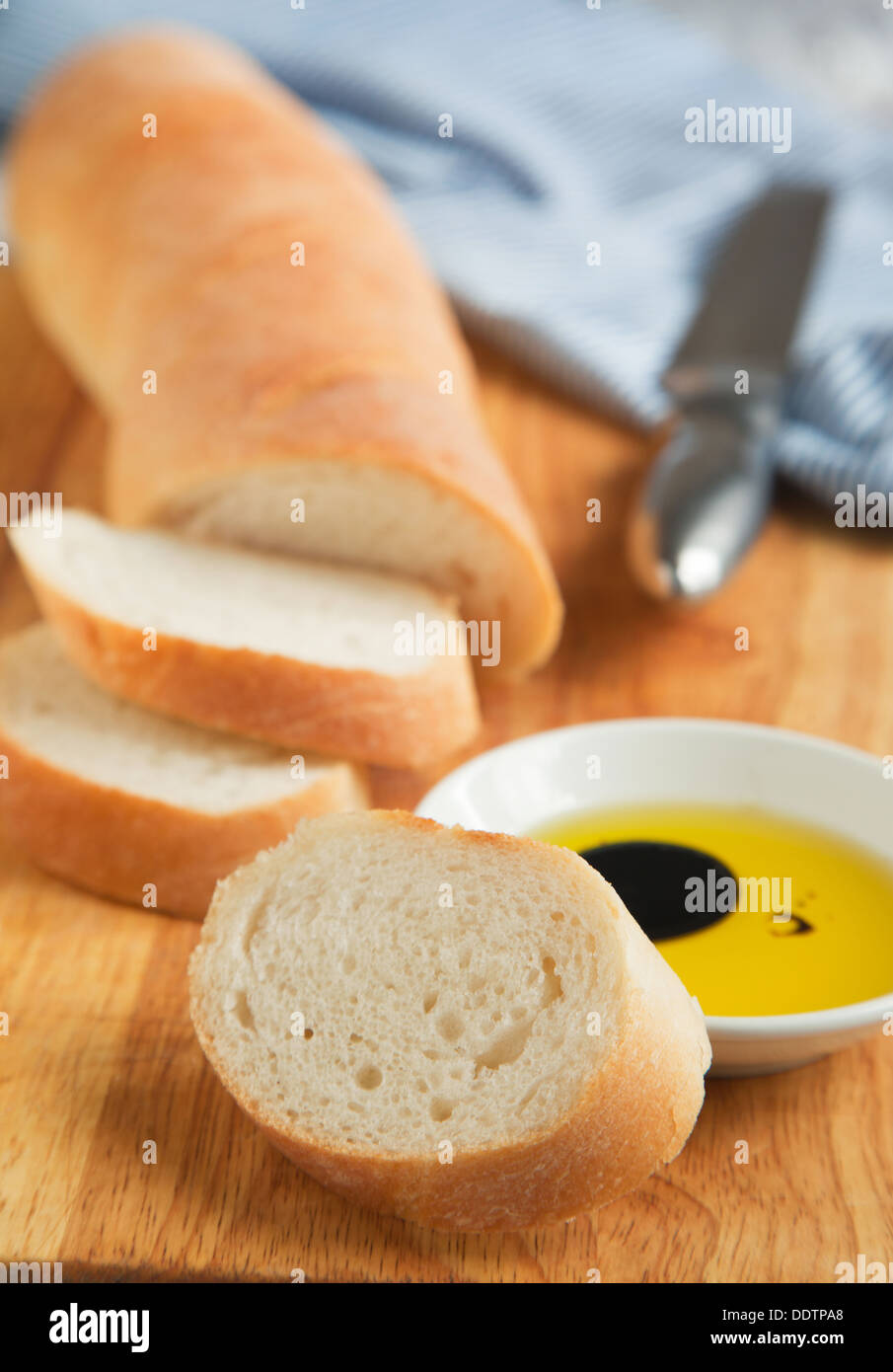 French bread baguette cut on wooden bread board and olive oil. Selective focus Stock Photo