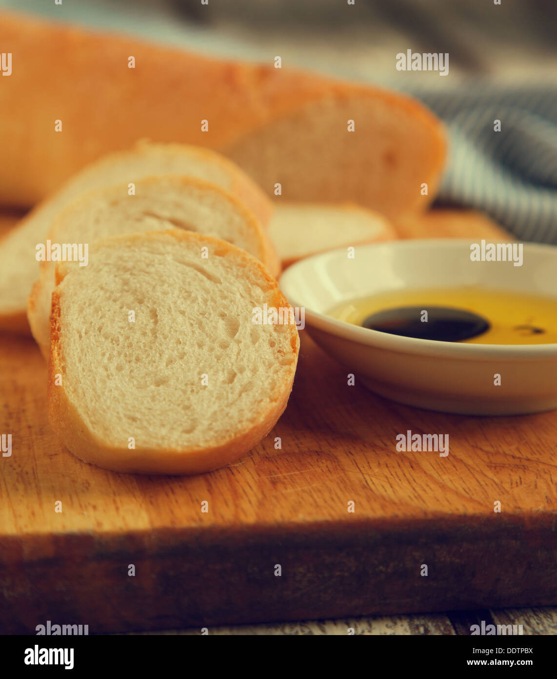 French bread baguette cut on wooden bread board and olive oil. Selective focus Stock Photo