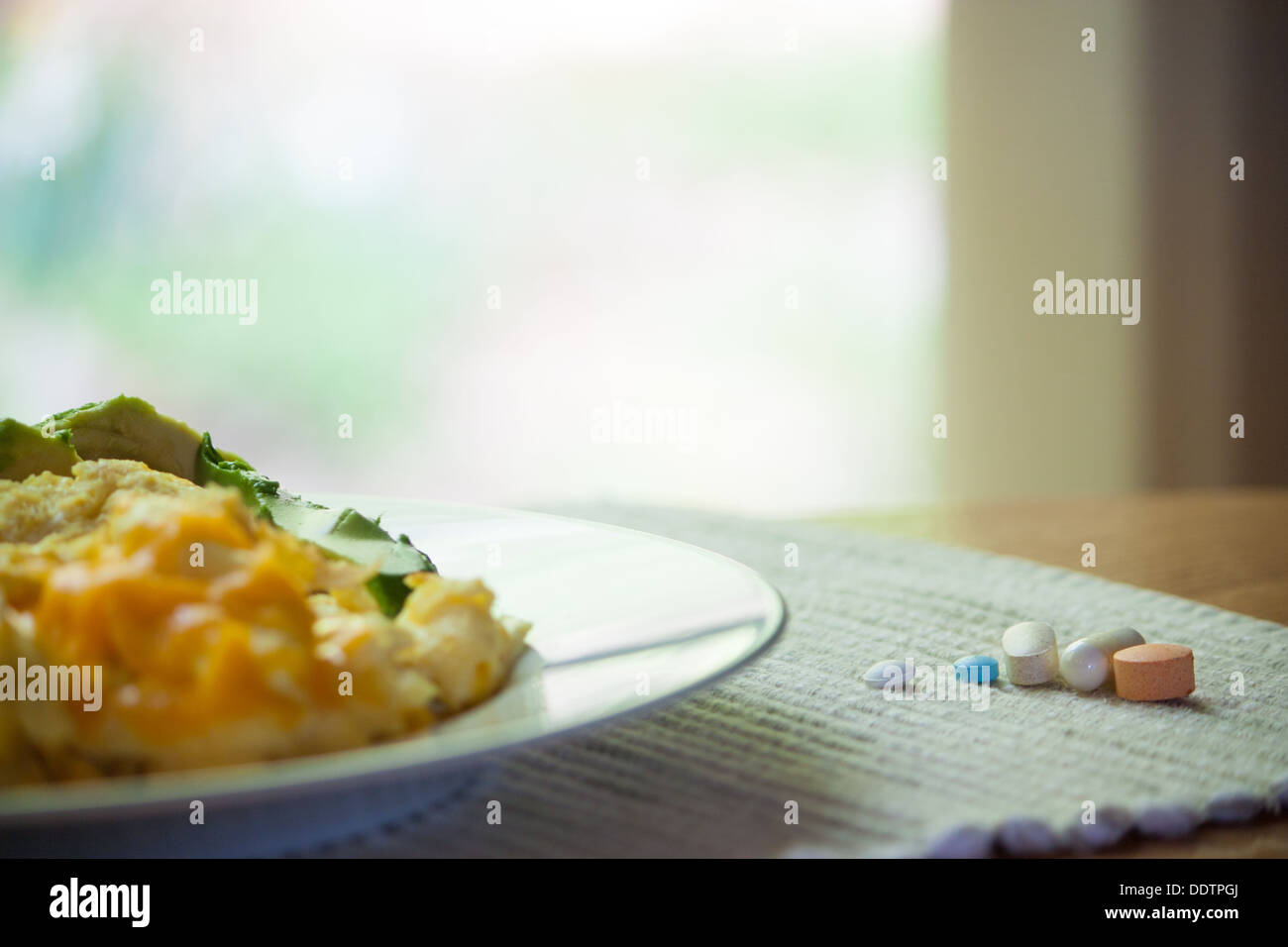 an aray of vitamins beside a breakfast of scrambled eggs florentine with cheese. Focus is on