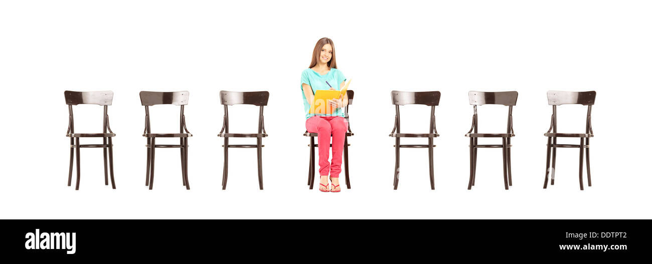 Smiling female student sitting on a wooden chair and writing notes ...