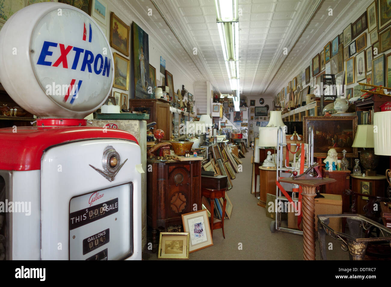 An old antique gas pump sits at the entrance of a cluttered antique