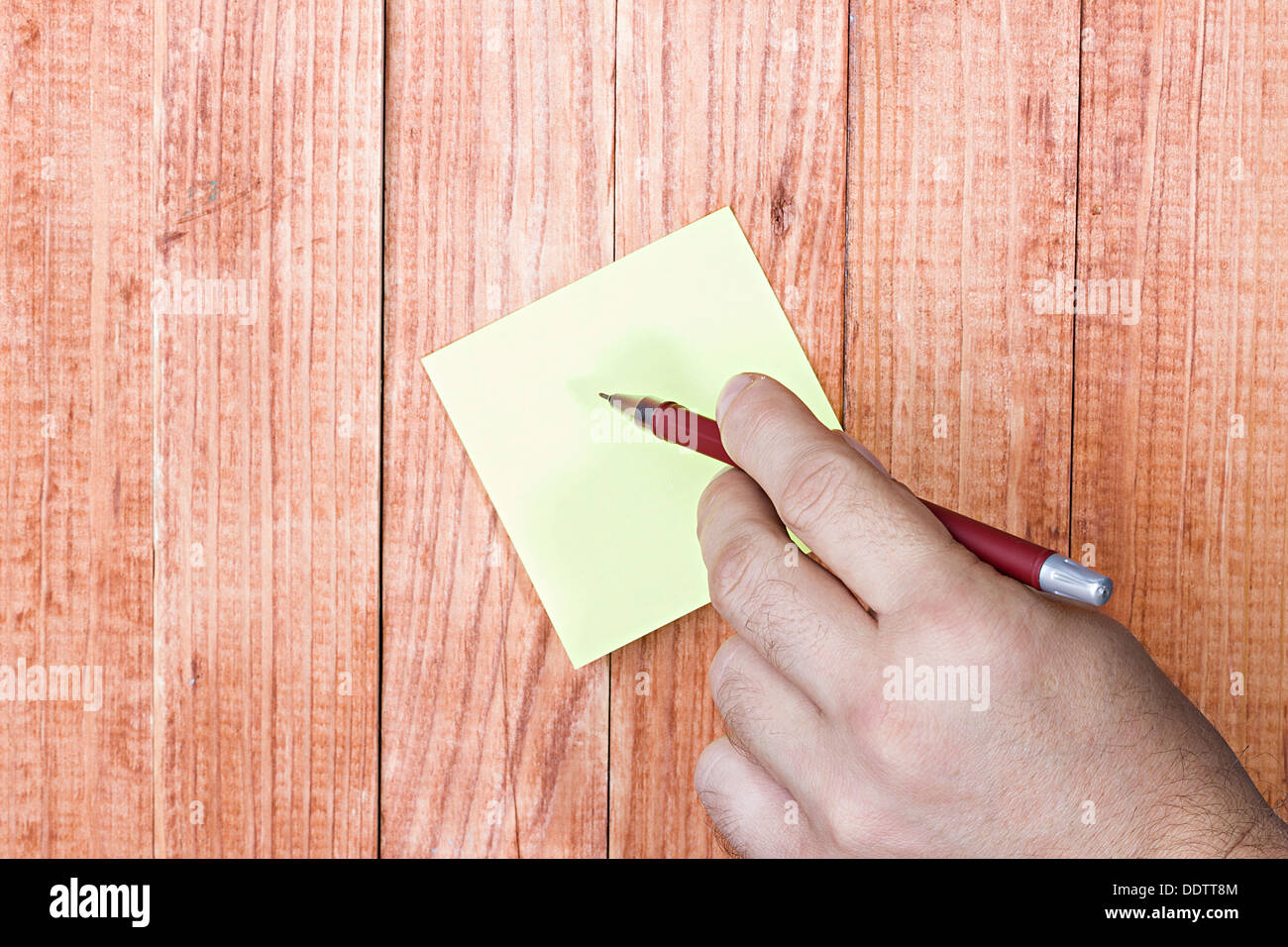 Blank note, paper stick, man's hand holding a pen, on wood background. Stock Photo