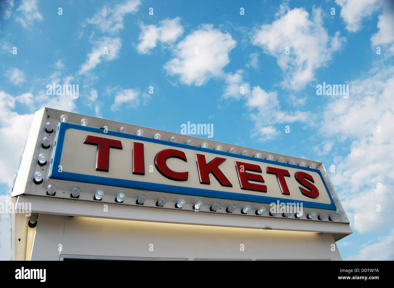 The word Tickets in red outlined with blue line and light bulbs against a blue sky with clouds. Stock Photo