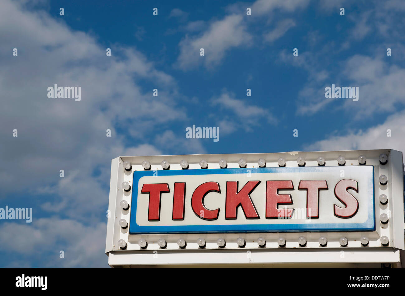 The word Tickets with light bulbs surrounding it as part of a ticket booth,on a blue sky white cloud background. Stock Photo