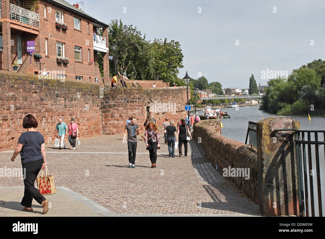 People walking along the riverside path close to the ancient city walls of Chester, England. Stock Photo