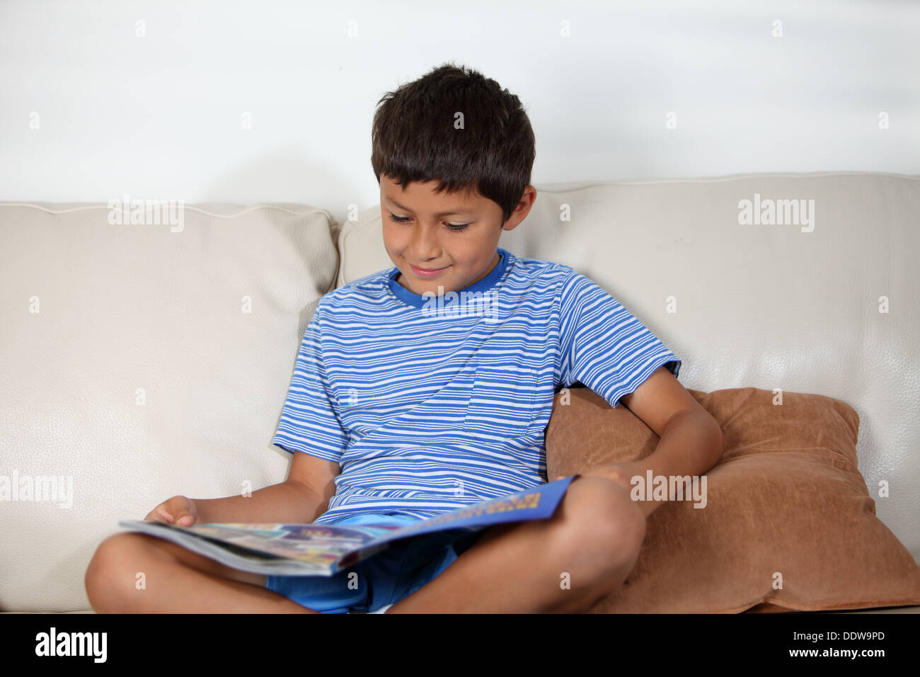Young boy on the sofa reading a magazine Stock Photo