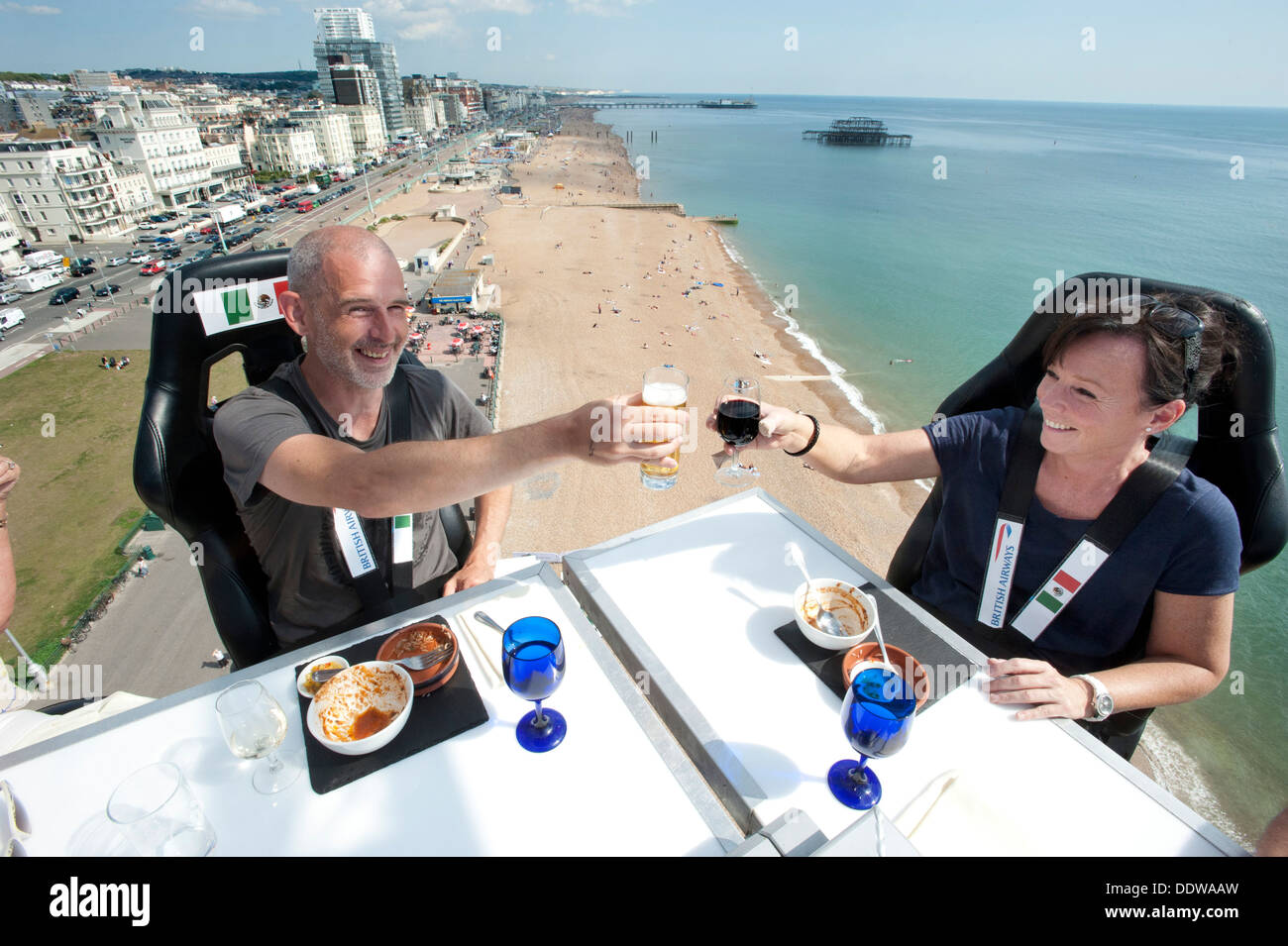 Diners enjoy eating at a high-flying dining table dangling from a crane 100 foot high in the sky above Brighton and Hove beach. Stock Photo