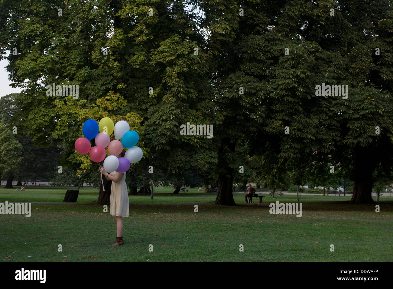 An anonymous girl stands holding a bunch of inflated balloons in a south London park. Stock Photo