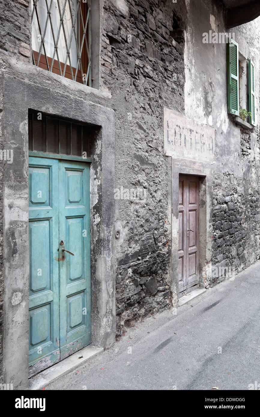 View of Italian village street with delapidated house wih fading paintwork on stone and stucco, old green wooden door, Northern Stock Photo