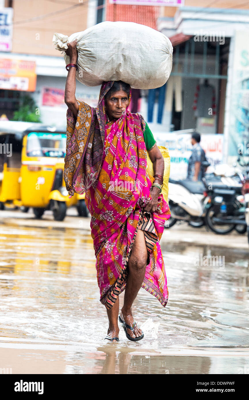 Elderly Indian woman carrying a sack on her head in the rain. Puttaparthi, Andhra Pradesh, India Stock Photo