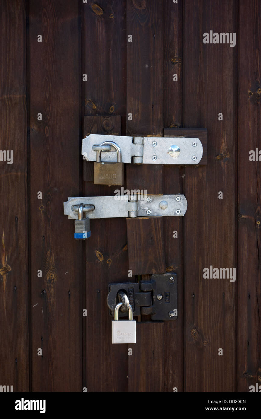 A closeup photo of three strong padlocks locking a wooden garage door