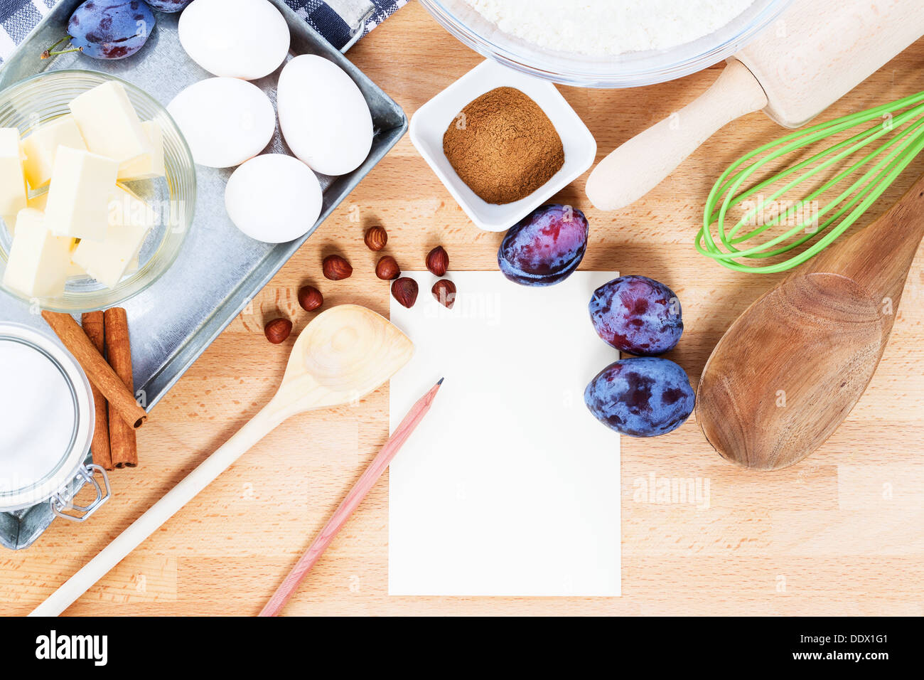 writing a recipe for plum cake with baking ingredients and tools from top with paper and a pencil Stock Photo