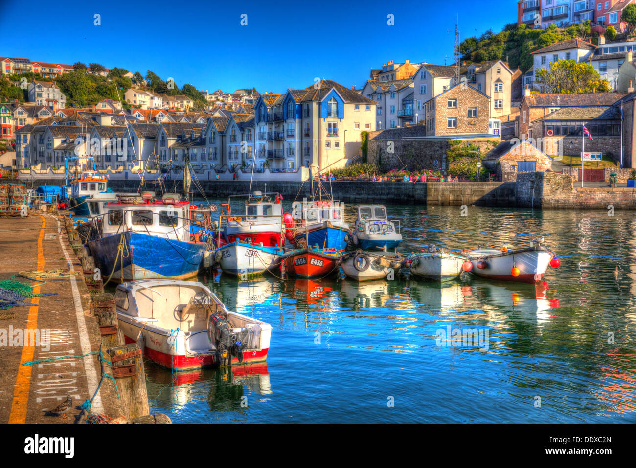 Fishing boats with bright colours Brixham harbour Devon with houses on hillside in background in HDR Stock Photo